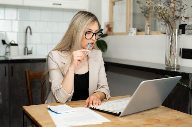 A person sitting at a desk with a laptop, reviewing documents related to mortgage refinancing options, with a pen in hand, looking thoughtful and engaged.