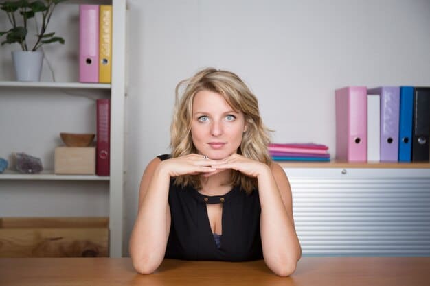 A close-up, eye-level shot of a young woman in her 20s sitting at a desk in a home office setup, smiling as she types on a laptop. The screen shows an affiliate marketing dashboard with various statistics and charts indicating successful conversions and earnings. The background is blurred, showcasing a bookshelf with marketing and business books, along with a small indoor plant, conveying a sense of dedication and success in online marketing.